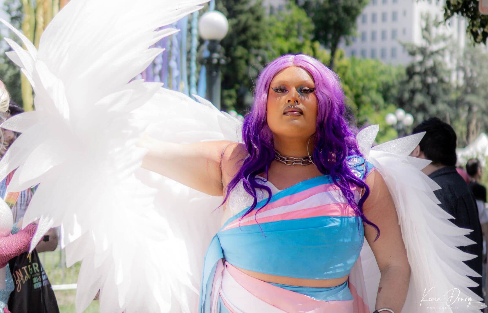 A person wearing a transgender pride colored outfit with wings at Denver PrideFest 2023