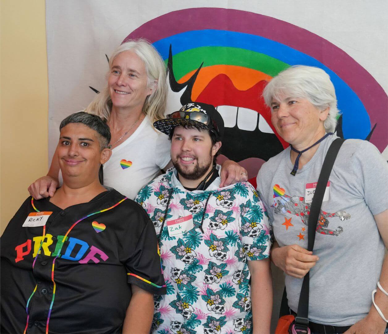 Four people pose for a photo in front of a rainbow backdrop at the 2023 Disability Pride Month celebration